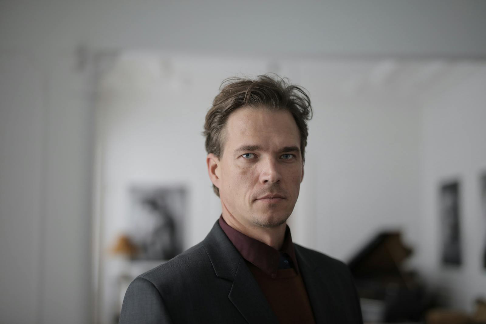 Confident businessman in a formal suit posing indoors with a serious expression.